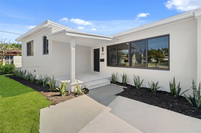 view of front facade featuring a front lawn, covered porch, and stucco siding