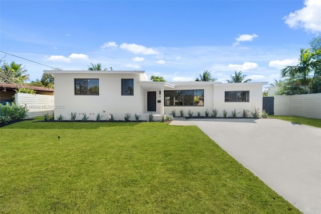 view of front facade with a front yard, concrete driveway, fence, and stucco siding