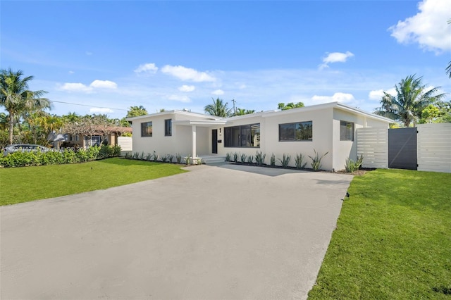 view of front facade featuring stucco siding, concrete driveway, a front yard, and a gate