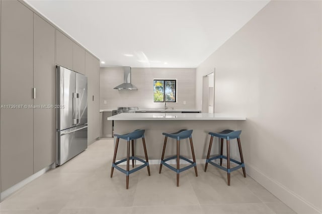 kitchen featuring wall chimney range hood, a breakfast bar, gray cabinets, a peninsula, and high quality fridge