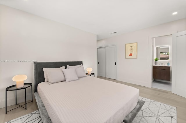 bedroom featuring visible vents, baseboards, ensuite bath, a closet, and light wood-type flooring