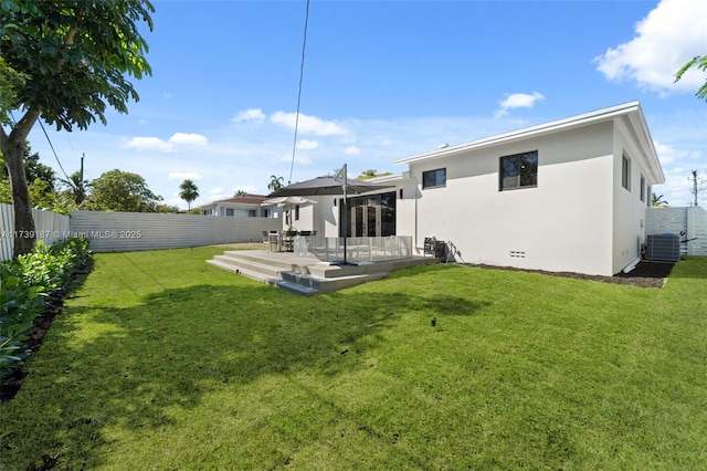 back of house featuring stucco siding, a lawn, central AC, and a fenced backyard