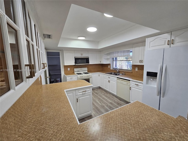 kitchen with visible vents, a sink, tasteful backsplash, white appliances, and a raised ceiling