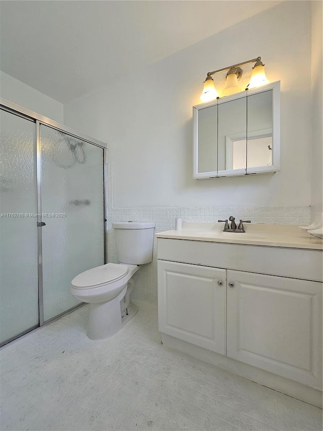 full bathroom featuring vanity, a wainscoted wall, a stall shower, tile walls, and toilet