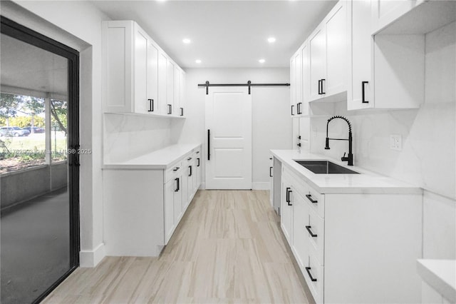 kitchen with a sink, a barn door, light countertops, and white cabinetry