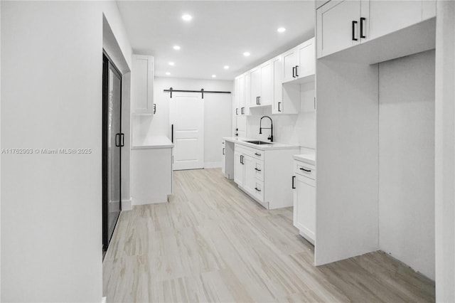 kitchen with a sink, recessed lighting, a barn door, light wood-style floors, and white cabinets