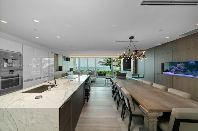 kitchen featuring light stone countertops, a sink, hanging light fixtures, wall oven, and modern cabinets