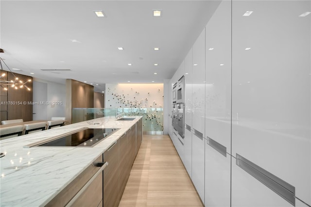 kitchen featuring light stone counters, white cabinets, modern cabinets, black electric cooktop, and a sink