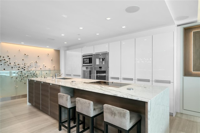 kitchen with appliances with stainless steel finishes, light wood-style floors, white cabinets, modern cabinets, and a sink