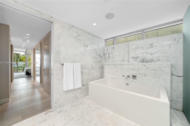 bathroom featuring ensuite bath, stone wall, a bath, and marble finish floor