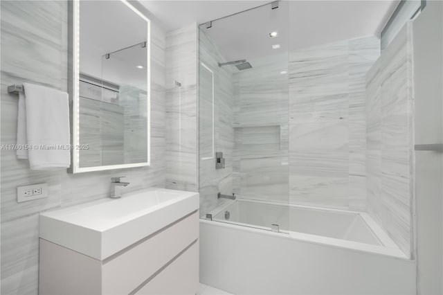 bathroom featuring bath / shower combo with glass door, tile walls, and vanity