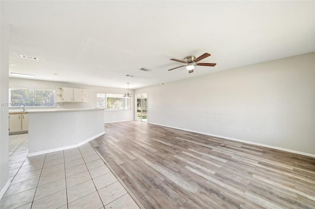 unfurnished living room featuring a sink, visible vents, light wood-style flooring, and ceiling fan with notable chandelier