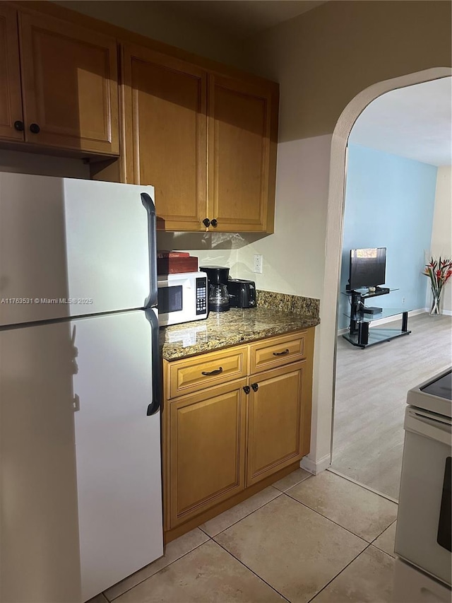 kitchen featuring white appliances, light tile patterned floors, baseboards, stone counters, and arched walkways