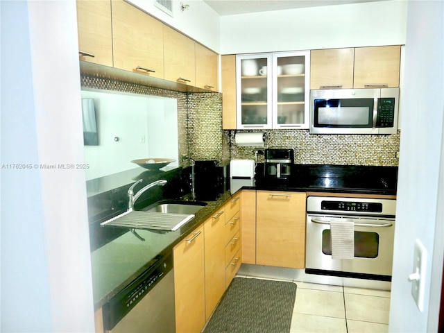 kitchen featuring backsplash, glass insert cabinets, appliances with stainless steel finishes, light tile patterned flooring, and a sink