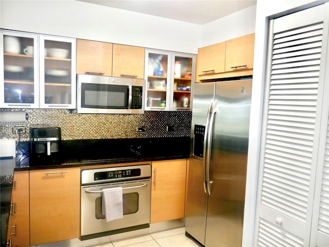 kitchen with glass insert cabinets, backsplash, appliances with stainless steel finishes, and light tile patterned flooring