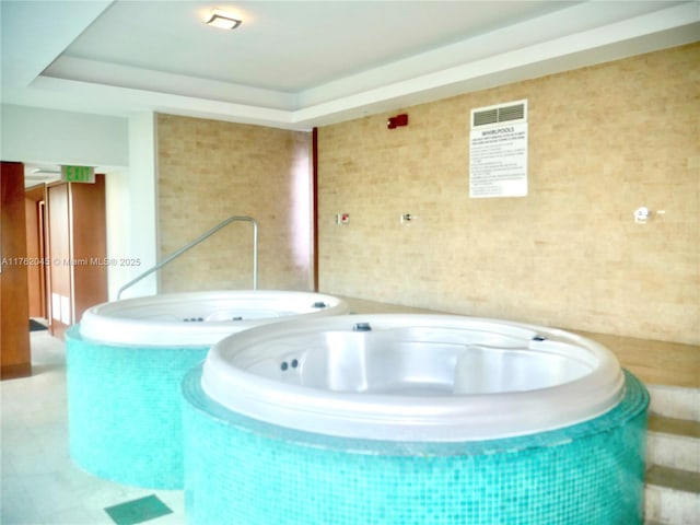 interior space featuring tile walls, a tub, and a raised ceiling