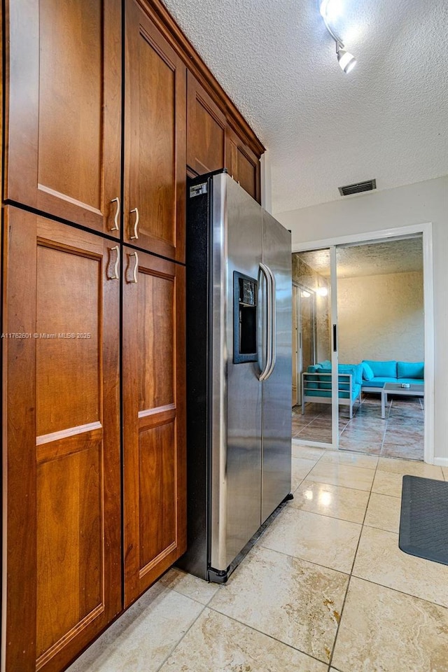 kitchen with brown cabinetry, visible vents, stainless steel refrigerator with ice dispenser, and a textured ceiling