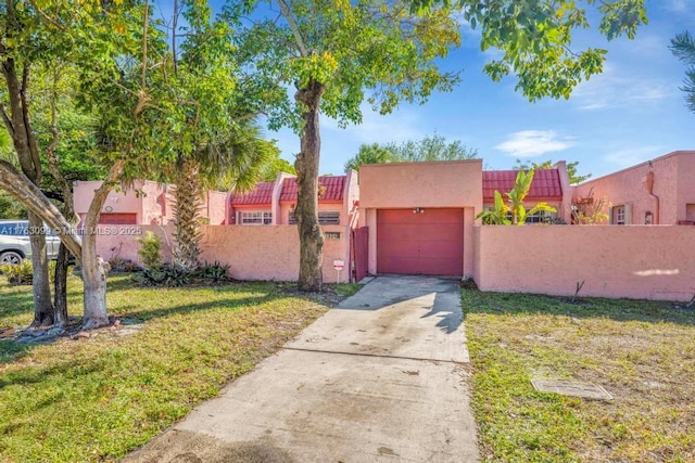 pueblo revival-style home with a front lawn, a fenced front yard, concrete driveway, stucco siding, and an attached garage