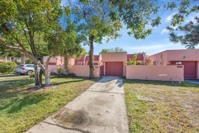 view of front of home with stucco siding, driveway, a fenced front yard, a front yard, and a garage