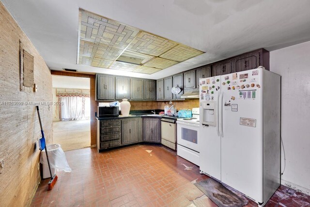 kitchen featuring under cabinet range hood, white appliances, brick floor, and a sink