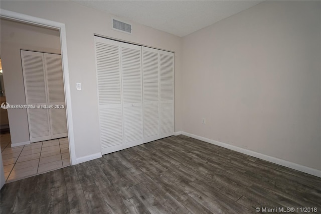 unfurnished bedroom with a closet, visible vents, baseboards, and wood finished floors