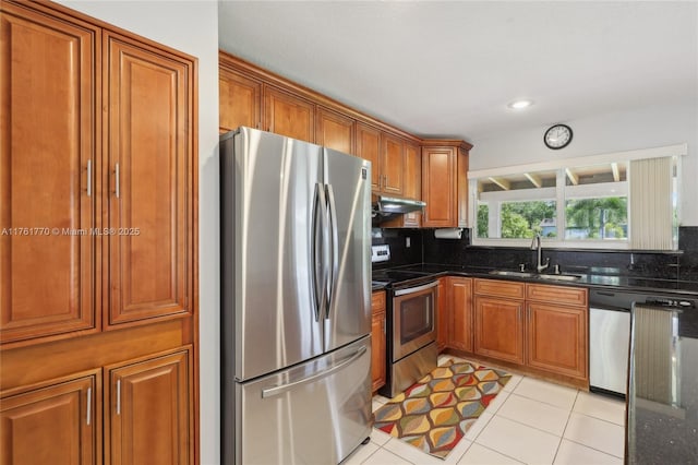 kitchen with a sink, under cabinet range hood, appliances with stainless steel finishes, brown cabinetry, and light tile patterned floors