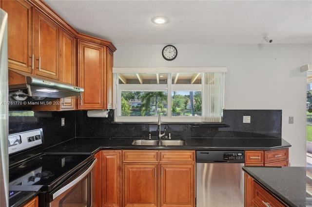 kitchen with backsplash, under cabinet range hood, appliances with stainless steel finishes, brown cabinetry, and a sink