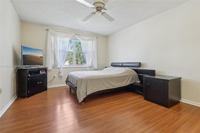 bedroom with baseboards, light wood-style flooring, a textured ceiling, and ceiling fan