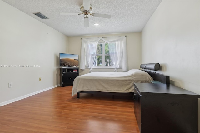 bedroom with visible vents, baseboards, a textured ceiling, and wood finished floors