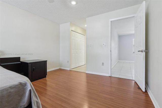 bedroom with a closet, a textured ceiling, baseboards, and wood finished floors