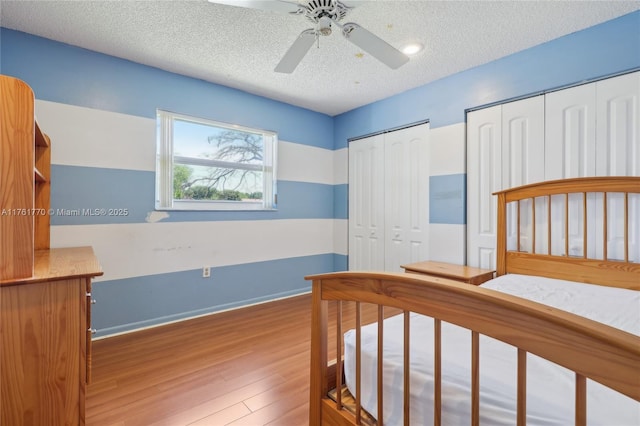 bedroom featuring ceiling fan, a textured ceiling, multiple closets, and wood finished floors