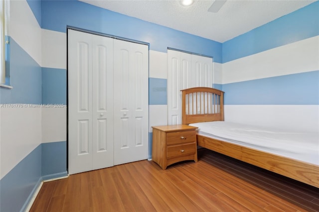 unfurnished bedroom featuring two closets, light wood-style floors, a ceiling fan, and a textured ceiling