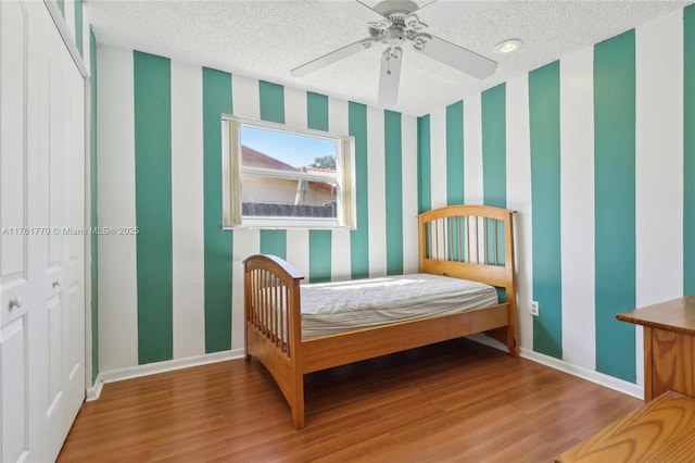 bedroom featuring baseboards, a textured ceiling, wood finished floors, and wallpapered walls