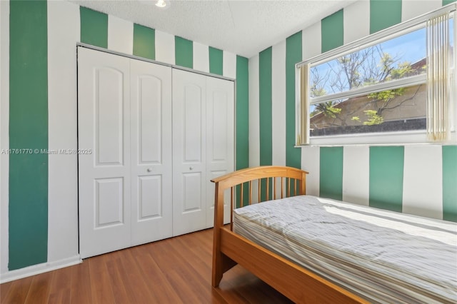 bedroom with a closet, a textured ceiling, wallpapered walls, and wood finished floors