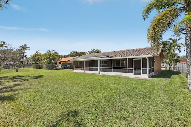 rear view of house featuring stucco siding, a tile roof, a fenced backyard, a yard, and a sunroom