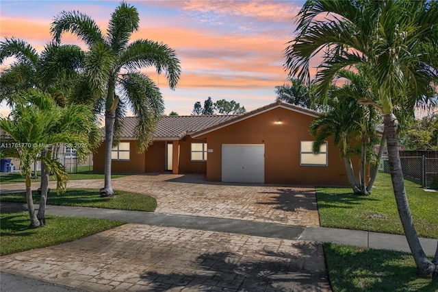 view of front facade with stucco siding, a tile roof, decorative driveway, fence, and an attached garage