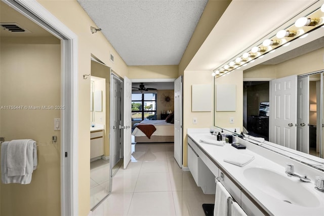 ensuite bathroom featuring connected bathroom, double vanity, tile patterned floors, a textured ceiling, and a sink