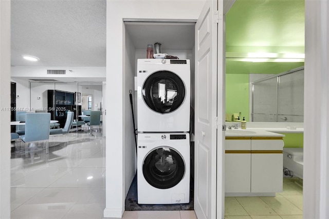 washroom featuring visible vents, light tile patterned floors, stacked washer and clothes dryer, a textured ceiling, and a sink