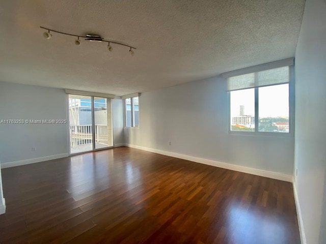 spare room with rail lighting, baseboards, a textured ceiling, and dark wood-style flooring