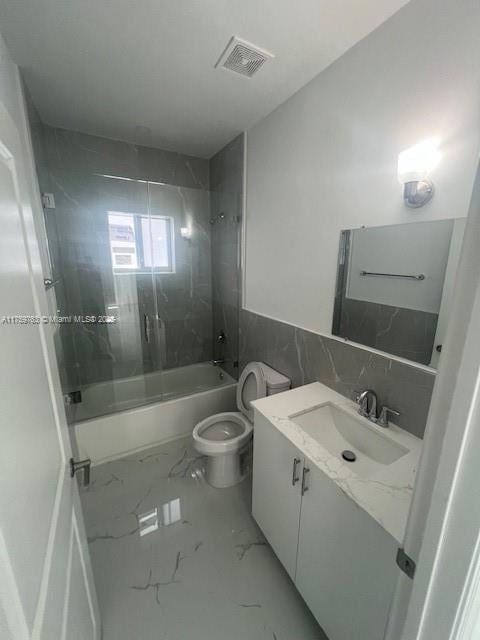 bathroom with visible vents, toilet, marble finish floor, combined bath / shower with glass door, and vanity