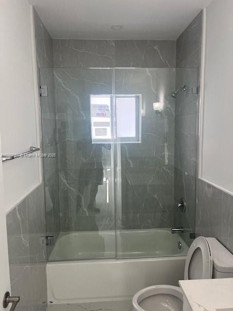 full bathroom with vanity, tile walls, toilet, and combined bath / shower with glass door