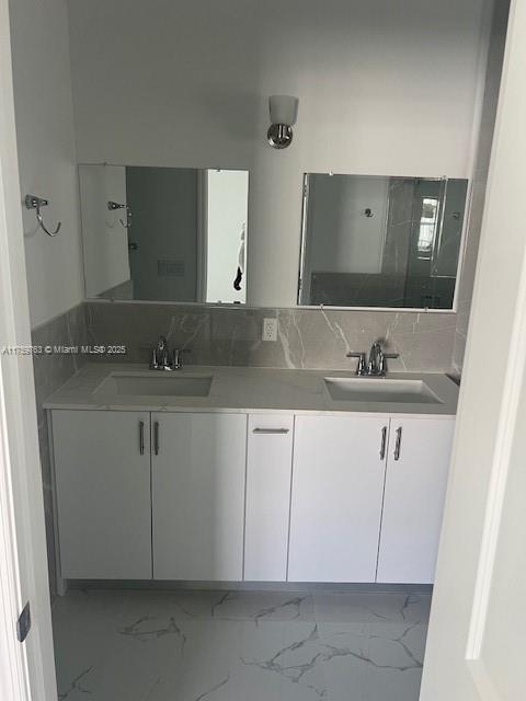 bathroom with double vanity, marble finish floor, tasteful backsplash, and a sink