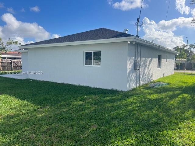 view of property exterior with a yard, fence, roof with shingles, and stucco siding