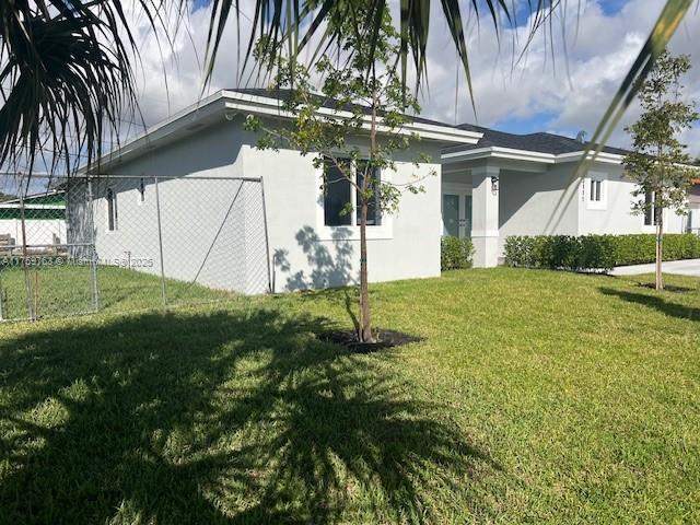 view of side of property with a lawn, fence, and stucco siding