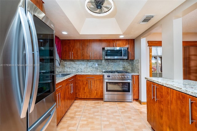 kitchen with visible vents, a tray ceiling, backsplash, appliances with stainless steel finishes, and light stone countertops