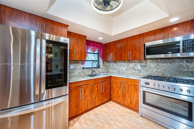 kitchen featuring a tray ceiling, light tile patterned floors, appliances with stainless steel finishes, and a sink