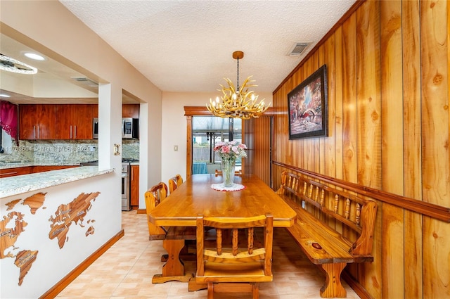 dining space with visible vents, baseboards, wood walls, a notable chandelier, and a textured ceiling