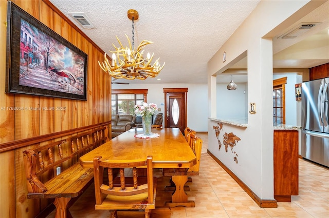 dining room featuring visible vents, a textured ceiling, a chandelier, and wood walls