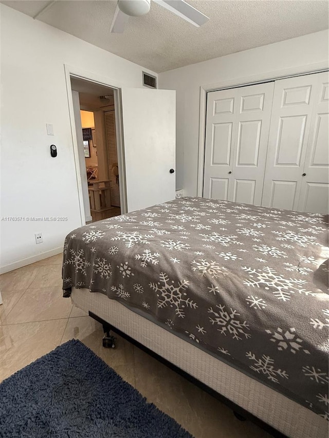 bedroom with visible vents, baseboards, ceiling fan, a closet, and a textured ceiling