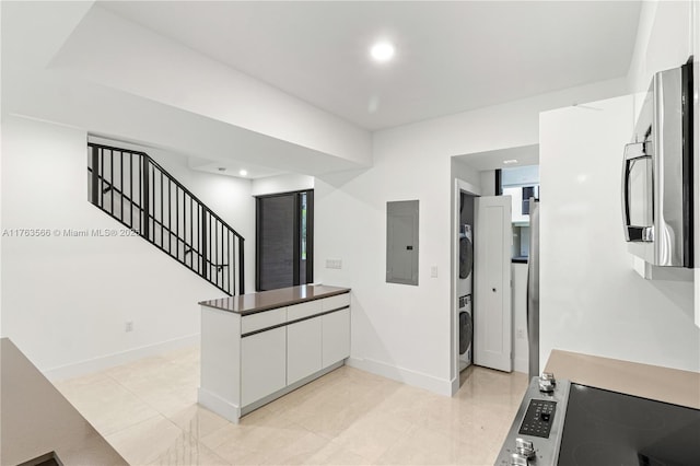 kitchen featuring a peninsula, electric panel, stainless steel appliances, white cabinets, and stacked washer and clothes dryer